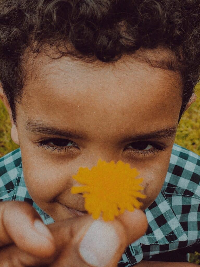 girl in blue and white checked shirt holding yellow flower